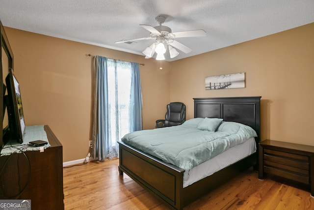 bedroom with light wood finished floors, a textured ceiling, a ceiling fan, and baseboards