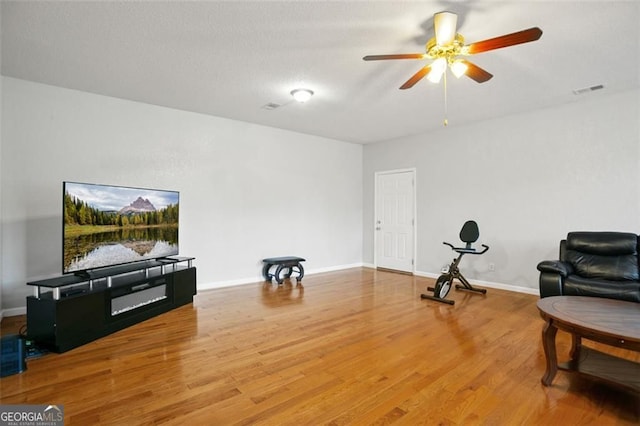 living area featuring wood finished floors, a ceiling fan, and baseboards