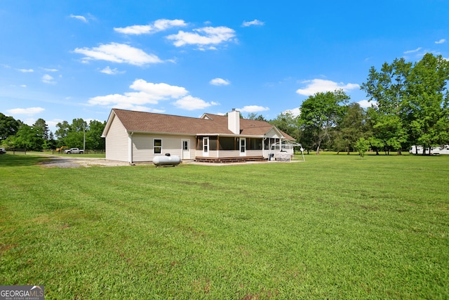 rear view of property with a lawn, a chimney, and a sunroom