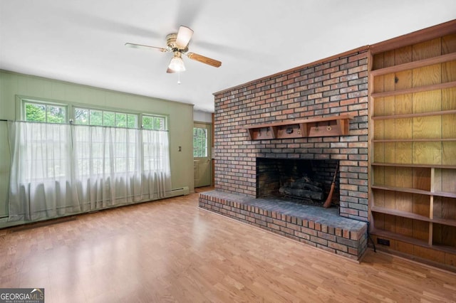 unfurnished living room featuring a ceiling fan, wood finished floors, a fireplace, and a baseboard heating unit