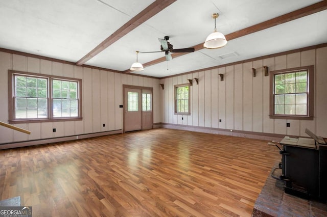 unfurnished living room with light wood-style floors, beam ceiling, a ceiling fan, plenty of natural light, and ornamental molding