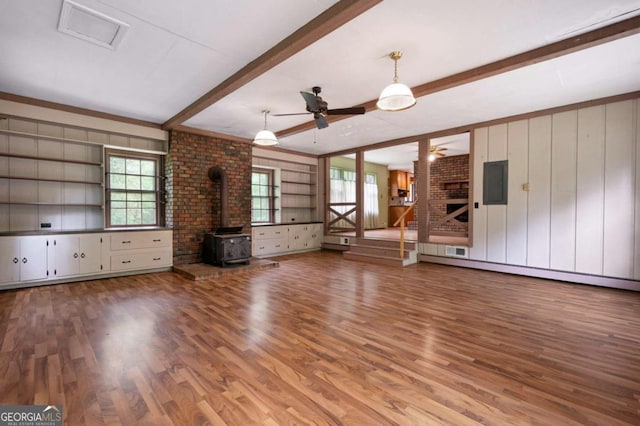 unfurnished living room with beamed ceiling, ceiling fan, a wood stove, wood finished floors, and plenty of natural light