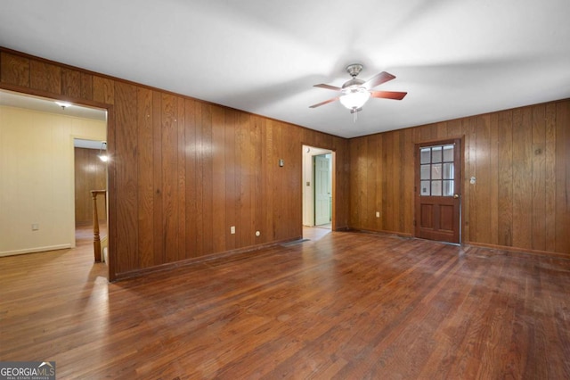 unfurnished living room featuring a ceiling fan, wood finished floors, wooden walls, and baseboards