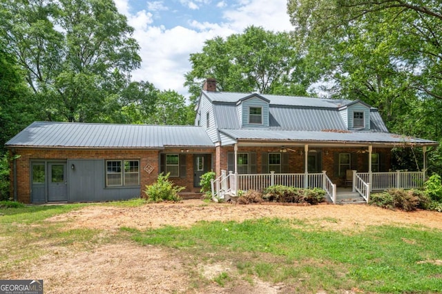 view of front of home featuring a chimney, metal roof, covered porch, brick siding, and a front lawn