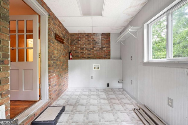 clothes washing area with tile patterned floors, hookup for a washing machine, brick wall, a wainscoted wall, and baseboard heating