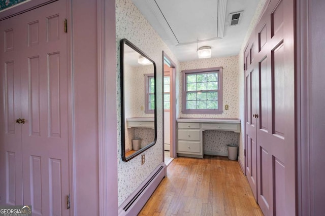hall with a baseboard radiator, wallpapered walls, attic access, and light wood-style floors