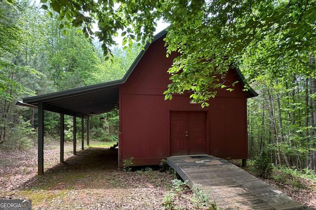 view of outbuilding with a carport, an outbuilding, and a wooded view