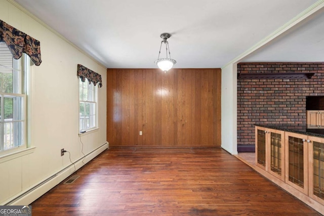 unfurnished dining area with a baseboard radiator, wood finished floors, wood walls, and ornamental molding