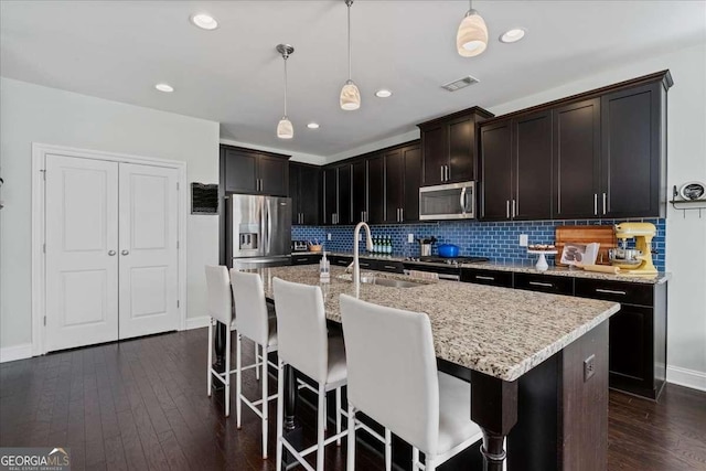 kitchen featuring appliances with stainless steel finishes, a sink, tasteful backsplash, decorative light fixtures, and light stone countertops