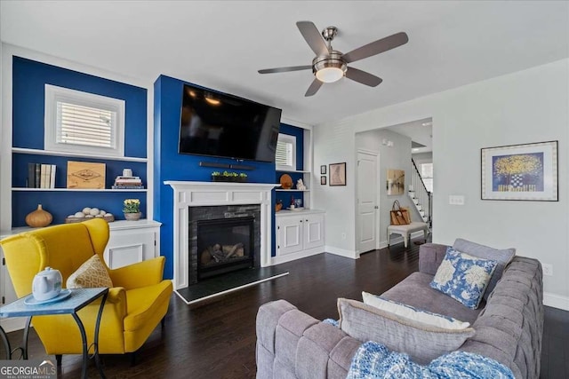 living area with wood finished floors, stairway, ceiling fan, a fireplace, and baseboards