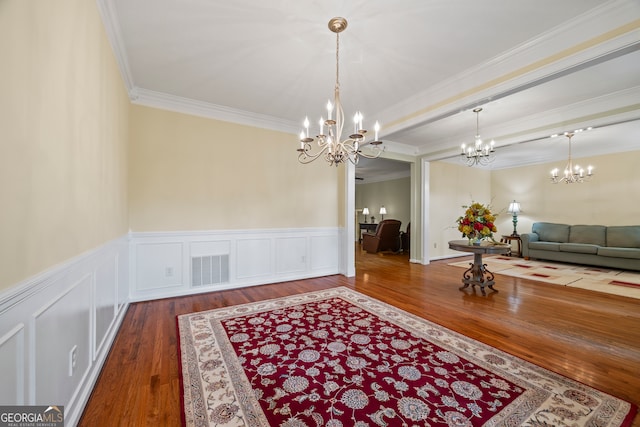 dining area featuring a chandelier, wood finished floors, crown molding, wainscoting, and a decorative wall