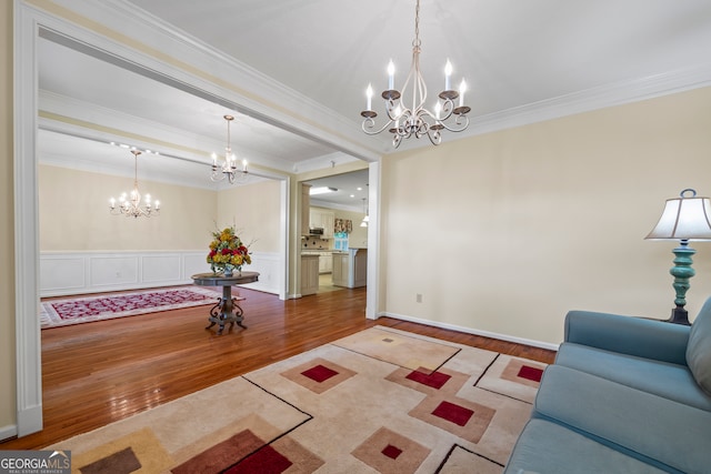 living area featuring a chandelier, wood finished floors, ornamental molding, and wainscoting