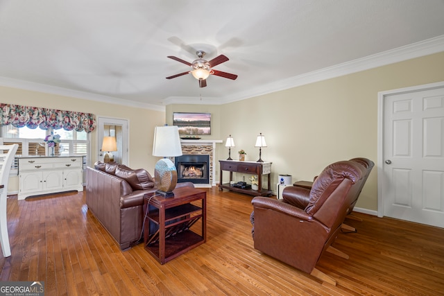 living area with crown molding, ceiling fan, a stone fireplace, and wood finished floors