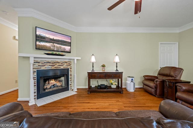 living area with ornamental molding, a ceiling fan, wood finished floors, a tile fireplace, and baseboards
