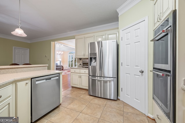 kitchen with stainless steel appliances, cream cabinetry, crown molding, light tile patterned floors, and hanging light fixtures