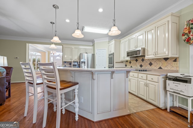 kitchen featuring appliances with stainless steel finishes, crown molding, cream cabinetry, a kitchen bar, and decorative backsplash