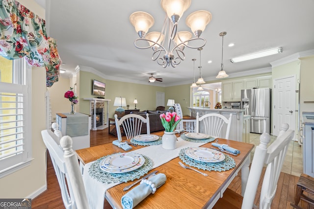 dining room with a ceiling fan, a fireplace, a chandelier, ornamental molding, and light wood-type flooring