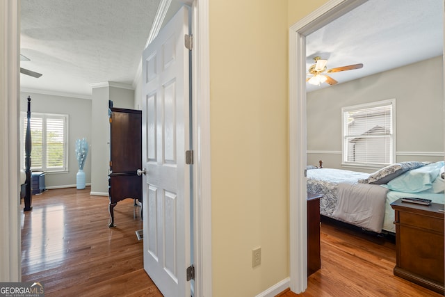 hallway featuring wood finished floors, a textured ceiling, ornamental molding, and baseboards