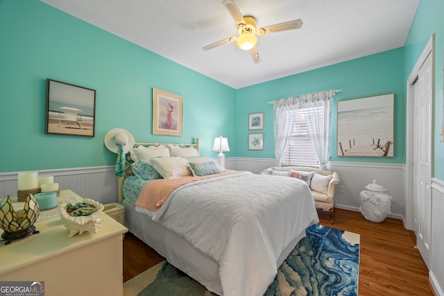 bedroom featuring a closet, wainscoting, wood finished floors, and a ceiling fan