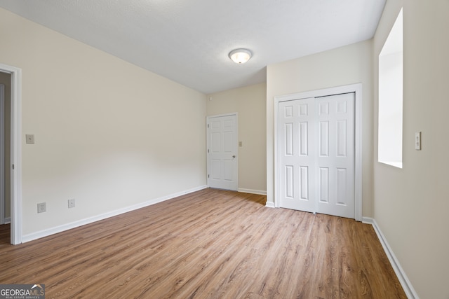 unfurnished bedroom featuring wood finished floors, baseboards, and a closet