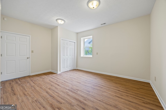 unfurnished bedroom featuring wood finished floors, baseboards, a closet, and a textured ceiling