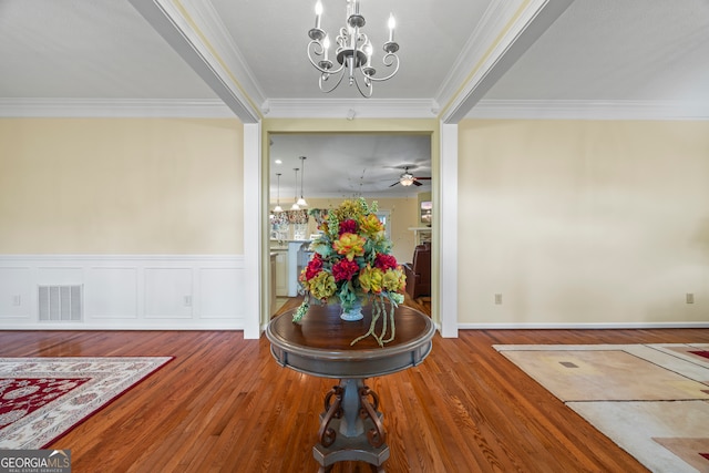 entryway with a chandelier, ornamental molding, wood finished floors, wainscoting, and ceiling fan