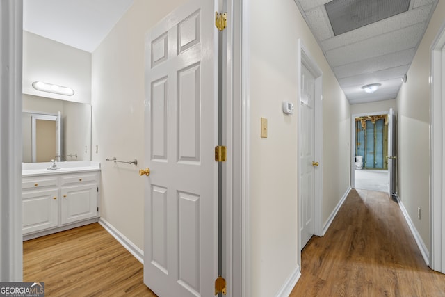 hallway with light wood-style flooring, baseboards, and a sink