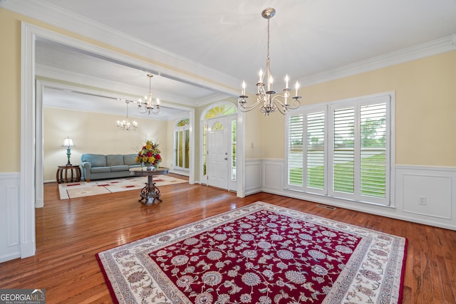 foyer entrance featuring a chandelier, wood finished floors, a wainscoted wall, ornamental molding, and a decorative wall