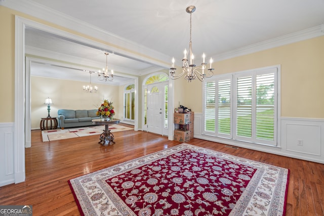 foyer with a chandelier, wood finished floors, ornamental molding, a wainscoted wall, and a decorative wall