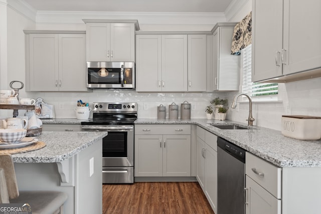 kitchen featuring appliances with stainless steel finishes, a sink, ornamental molding, decorative backsplash, and light stone counters