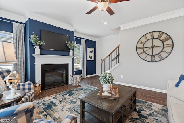 living area featuring a ceiling fan, crown molding, a glass covered fireplace, baseboards, and wood finished floors