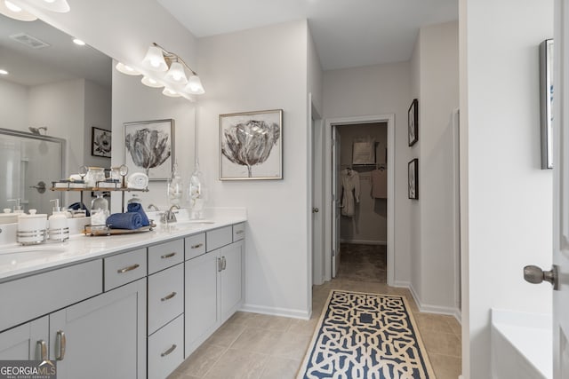 full bathroom with tile patterned floors, a stall shower, a walk in closet, double vanity, and baseboards