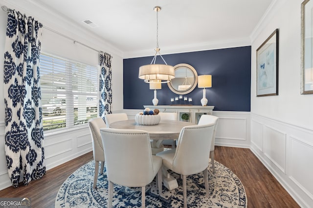 dining area with dark wood-type flooring, a decorative wall, crown molding, and wainscoting