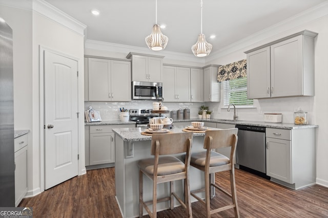 kitchen with stainless steel appliances, gray cabinetry, a sink, a kitchen bar, and crown molding