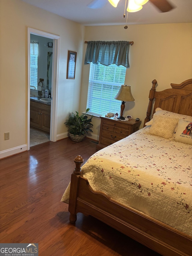 bedroom with dark wood-style floors, baseboards, ensuite bath, and a ceiling fan