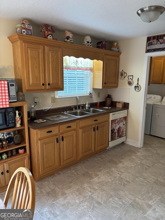 kitchen with a sink, black microwave, washing machine and dryer, white dishwasher, and dark countertops