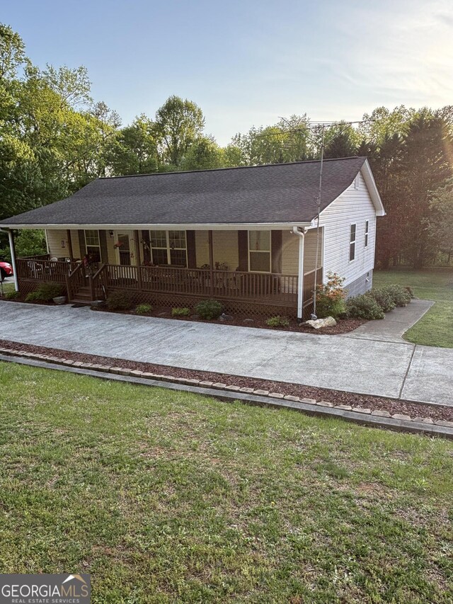 view of front of house with covered porch, driveway, a front lawn, and a shingled roof