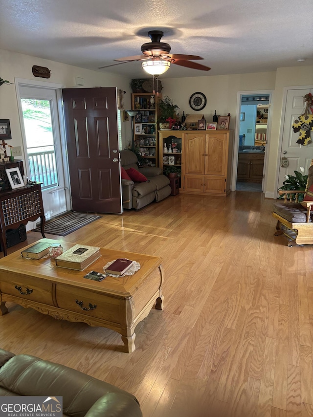 living room featuring light wood-style floors, a ceiling fan, and a textured ceiling