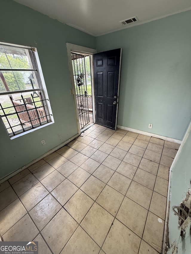 empty room with light tile patterned floors, baseboards, and crown molding