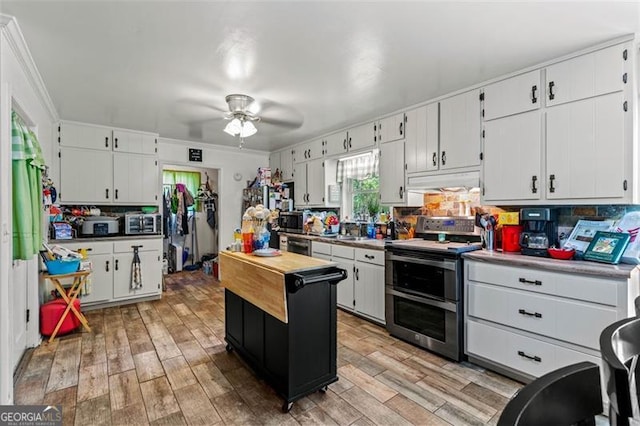 kitchen with stainless steel appliances, under cabinet range hood, a ceiling fan, light wood-type flooring, and white cabinetry