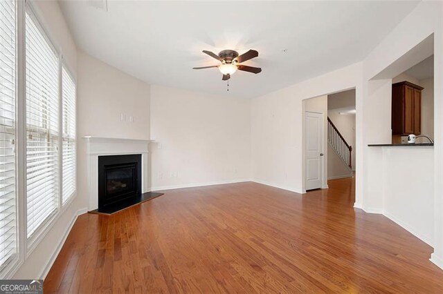 1957 Brightleaf Way Unit 59, Marietta, GA 30060 - unfurnished living room featuring ceiling fan, wood finished floors, a glass covered fireplace, stairway, and baseboards