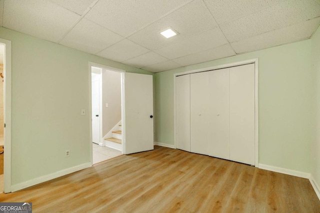 unfurnished bedroom with a paneled ceiling, wood finished floors, baseboards, and a closet