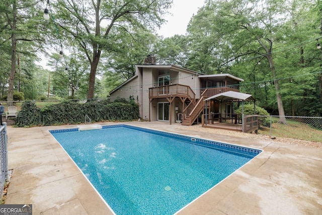 view of pool featuring fence, a wooden deck, stairs, a patio area, and view of scattered trees