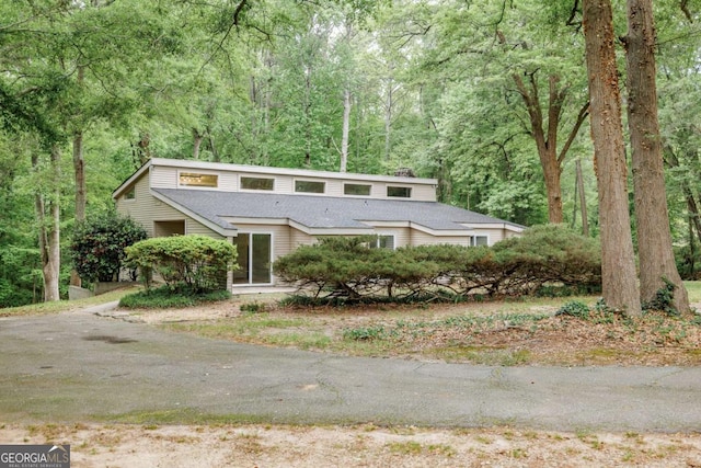 mid-century home featuring roof with shingles and a wooded view