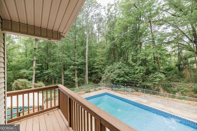 view of swimming pool with a fenced backyard, a wooden deck, and a forest view