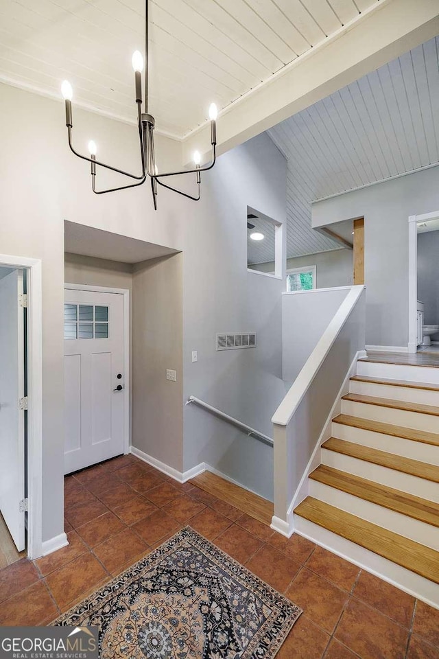 tiled entrance foyer with baseboards, a chandelier, and stairs