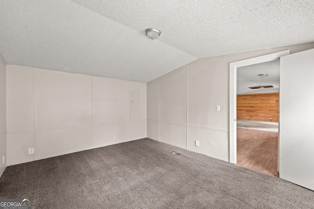 carpeted empty room featuring a textured ceiling, vaulted ceiling, and a decorative wall
