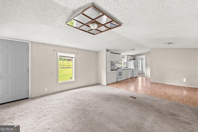 unfurnished living room featuring a textured ceiling, light carpet, light wood-type flooring, and vaulted ceiling