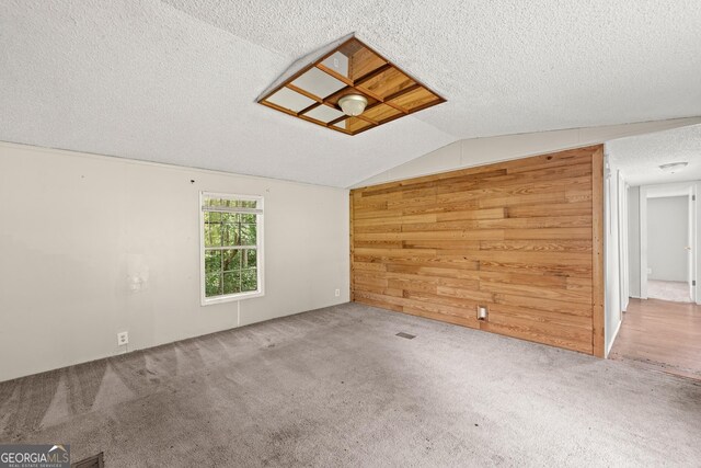 spare room with a textured ceiling, wooden walls, carpet, and lofted ceiling