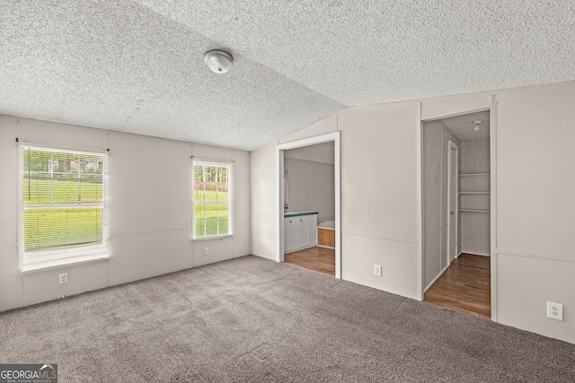 unfurnished bedroom with carpet, a textured ceiling, lofted ceiling, and ensuite bath